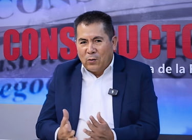 Luis Villanueva Carbajal en el set del programa El Constructor con manos abiertas explicando, camisa blanca y saco azul.