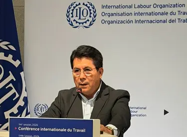 Luis Villanueva en saco y camisa dando discurso en la OIT
