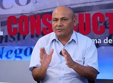 Jhon Irene Gonzales con camisa celeste manga corta frente a un banner del set que dice El Constructor